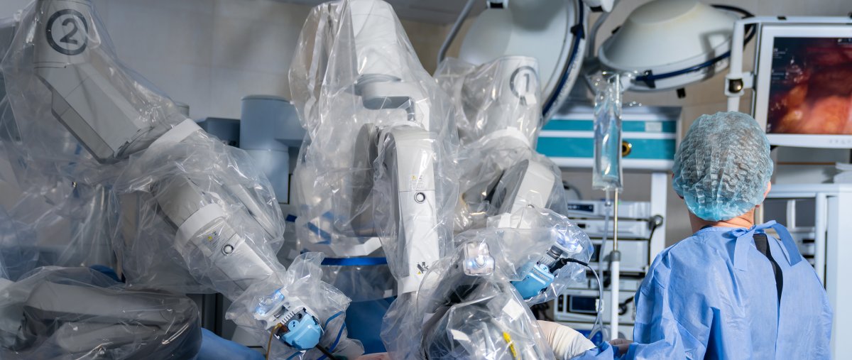 Surgeon in a surgical suite using a robot-assisted surgical device while looking at a medical-grade display showing the surgery.