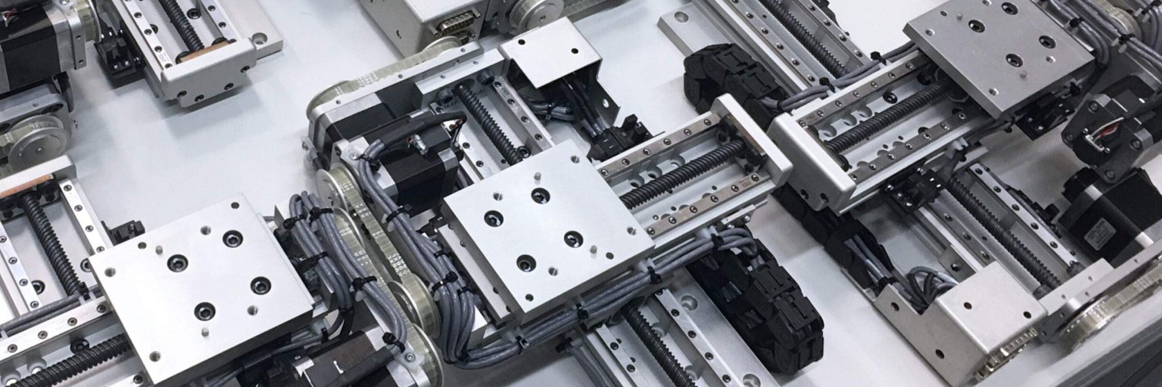 Overhead view of multiple precision linear motion assemblies with lead screws, metal guide rails, motors, and bundled wiring arranged in a clean industrial automation system.