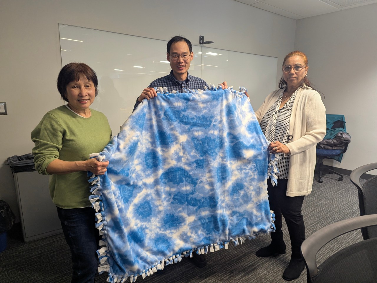 Three Novanta employees holding up one of the no-sew blankets they made