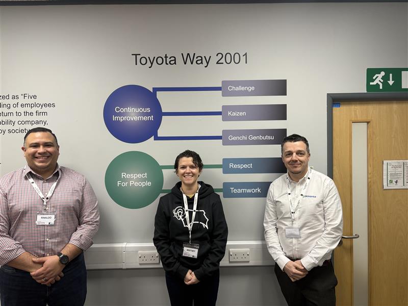 Three Novanta employees standing in front of a wall at Toyota with "The Toyota Way" printed on the wall.