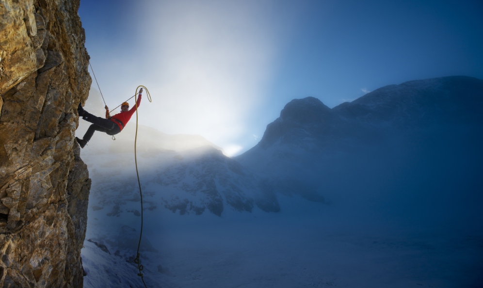 Mountain climber on the side of a cliff with a blue mountainous landscape behind him